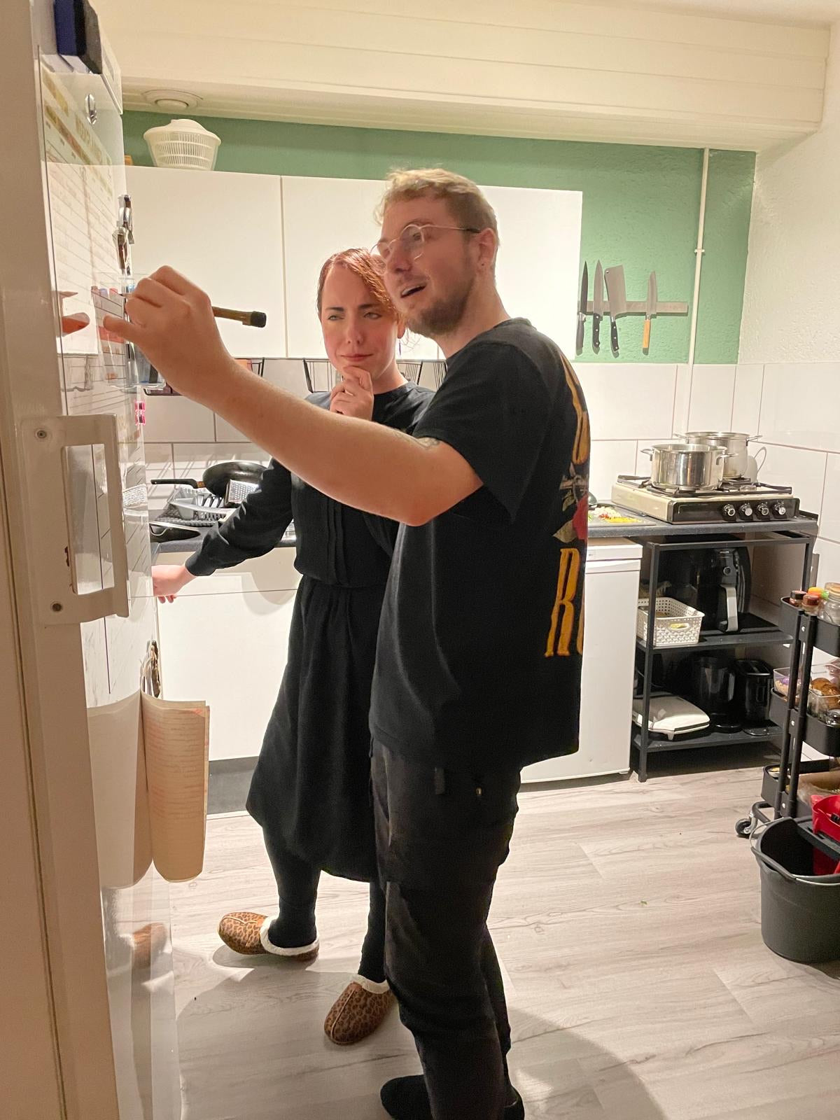 Stel vult samen de weekplanner in die aan de muur van hun keuken hangt